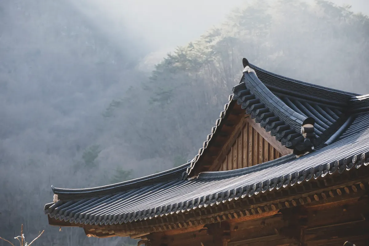 A traditional Korean temple roof with mountains in the background, capturing the serene winter landscape.